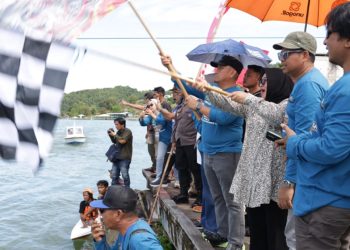 Bupati Luwu Timur, Irwan Bachri Syam dan Wabup Lutim, Puspwati mengangkat bendera start tanda dimulainya Lomba Perahu bala-Bala di Anjungan Sungai Malili. (Foto: Kominfo SP Lutim)