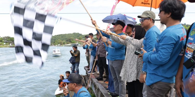 Bupati Luwu Timur, Irwan Bachri Syam dan Wabup Lutim, Puspwati mengangkat bendera start tanda dimulainya Lomba Perahu bala-Bala di Anjungan Sungai Malili. (Foto: Kominfo SP Lutim)
