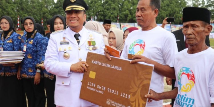 Bupati Luwu Timur, Irwan Bachri Syam, menyerahkan secara simbolis Kartu Lansia kepada perwakilan warga berusia di atas 60 tahun pada peringatan HUT ke-80 RI di Lapangan Pendidikan, Malili, Minggu (17/08/2025). (Foto: Chullank_art)